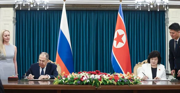 Cérémonie de signature d'accords entre la Russie et la Corée du Nord, drapeaux des deux pays en arrière-plan.