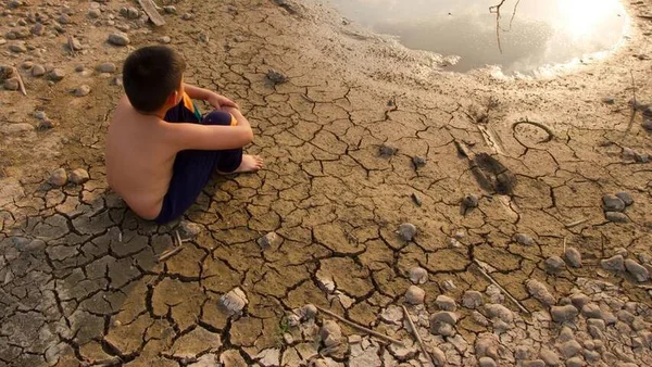 Un garçon assis sur la terre desséchée d'un réservoir en baisse, symbole de la sécheresse frappant les enfants.