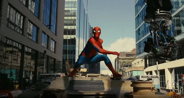 En coulisses : un cascadeur en costume Spider-Man sur un toit, avec une caméra de tournage.