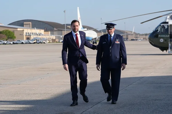 J.D. Vance et un officier militaire marchant sur un tarmac, avec hélicoptère en arrière-plan.
