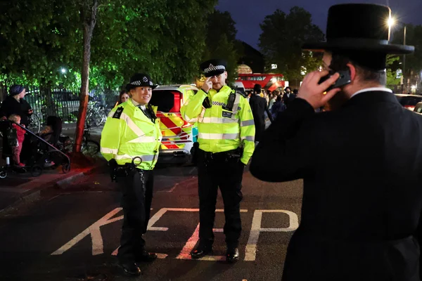 Des policiers londoniens patrouillent de nuit devant un homme de la communauté juive orthodoxe.
