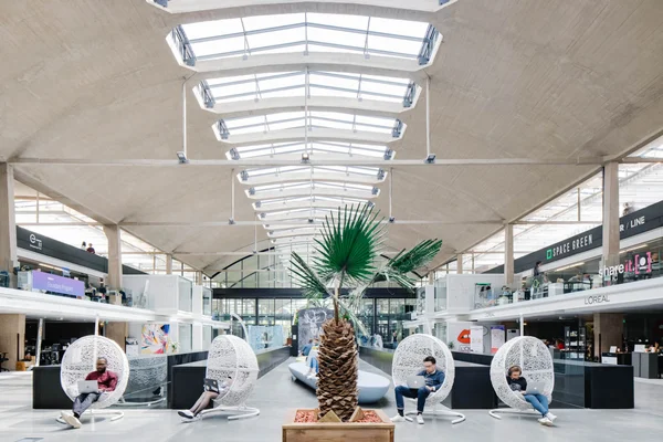 Des entrepreneurs travaillant dans les célèbres fauteuils suspendus de Station F, avec les logos d'entreprises partenaires en arrière-plan.