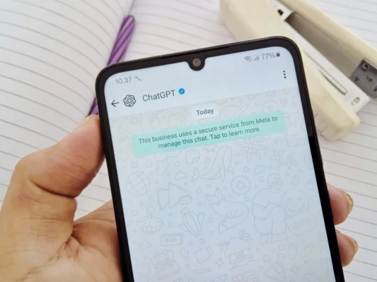 Capture d'écran d’une conversation WhatsApp avec ChatGPT, posée sur un bureau.