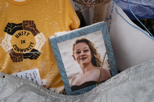 Mémorial pour Renee Good recouvert de neige, avec son portrait et un t-shirt symbolique 'UNITY IN COMMUNITY'.