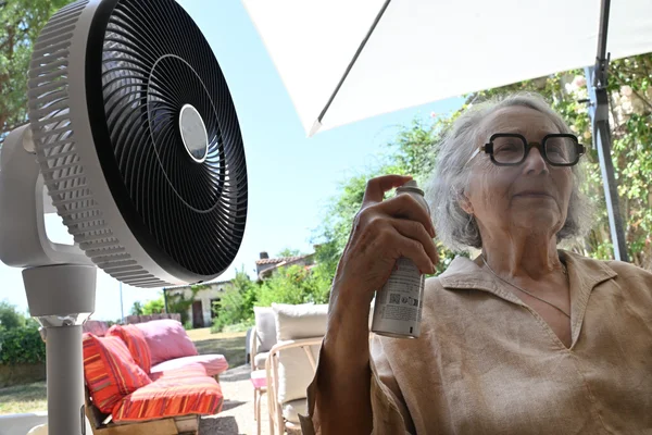 Une personne utilisant un ventilateur et un spray pour se rafraîchir durant la canicule.