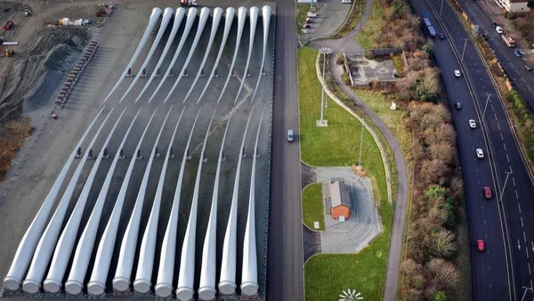 Vue aérienne d'une usine de pales d'éoliennes avec des rangées parallèles de pales blanches.