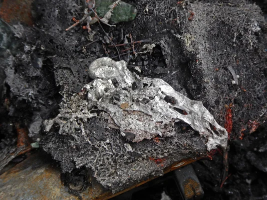 Restes d'une voiture incendiée, métal fondu et débris carbonisés.