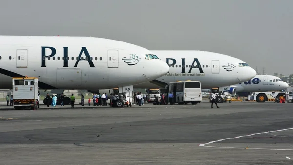 Des avions de Pakistan International Airlines (PIA) sur un tarmac, des passagers embarquant via une passerelle mobile.
