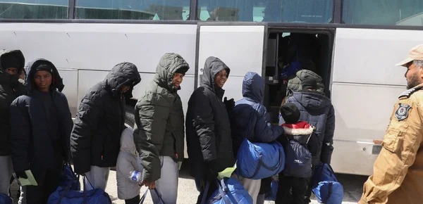 Migrants embarquant dans un bus sous la supervision d'un agent en uniforme en Libye.