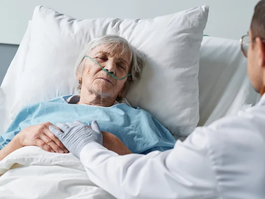 Patiente âgée en soins palliatifs, maintenue par un soignant.