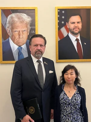 Un diplomate et une femme devant des portraits de Donald Trump et J.D. Vance.