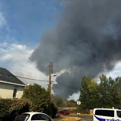 Un important panache de fumée noire s'élève au-dessus d'un quartier résidentiel de Nantes lors de l'incendie d'un camp de Roms, avec des véhicules de police en intervention.