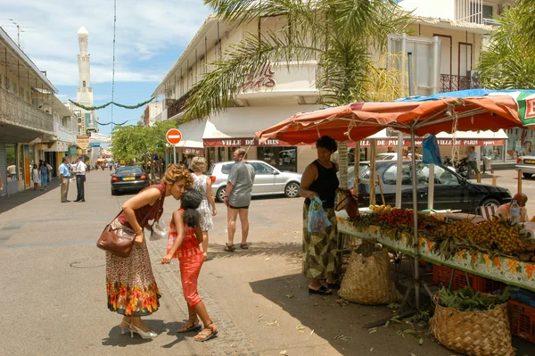Scène de rue à La Réunion avec un étal de fruits et une mosquée en arrière-plan.