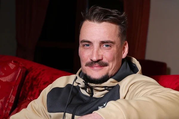 Pierre Lottin posant sur un canapé rouge, vêtu d'une veste à capuche.
