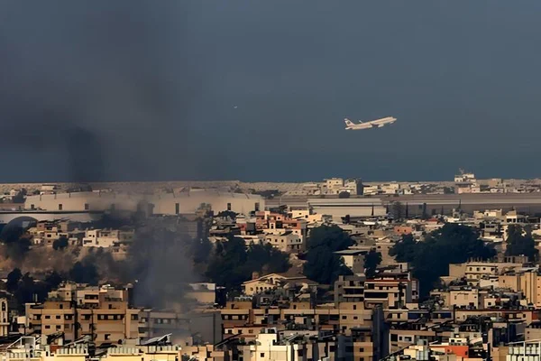 Vue d'une ville avec de la fumée s'élevant de bâtiments et un avion en vol.