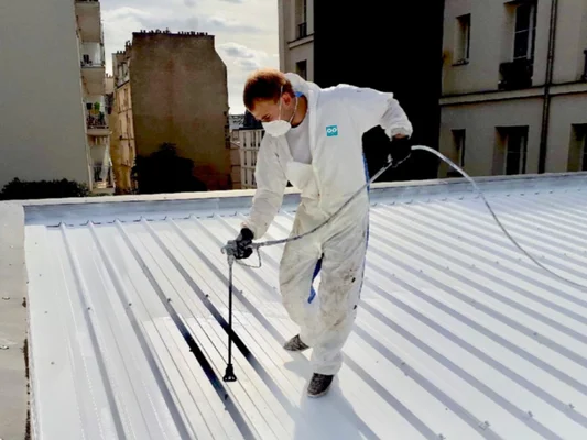 Peinture blanche appliquée sur un toit en tôle par un professionnel, une solution contre la canicule.