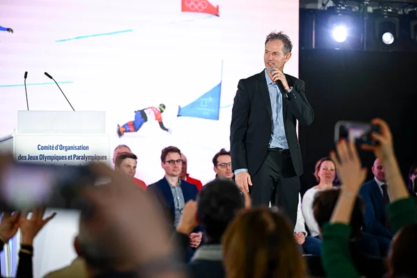 Un responsable s'exprimant lors d'une conférence, avec en arrière-plan l'écran du comité Paris 2024.