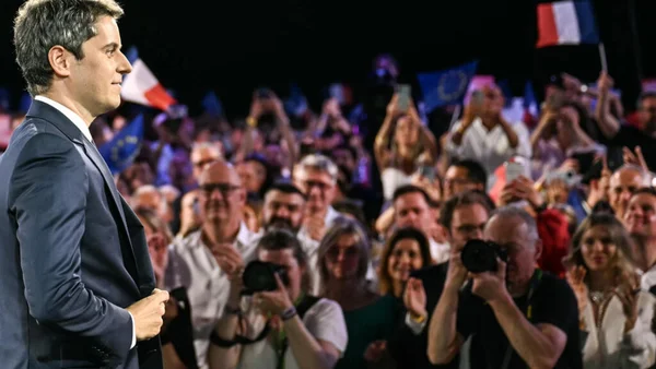 Meeting de campagne présidentielle : un candidat s'adresse à une foule de supporters brandissant des drapeaux français et européens.