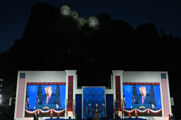 Meeting politique au Mont Rushmore : un orateur s'adresse à la foule devant les visages illuminés des présidents américains.
