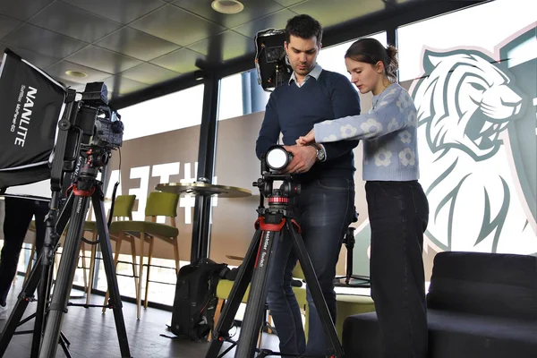 Duo de techniciens ajustant une caméra en studio, avec éclairage professionnel et logo tigre en arrière-plan.