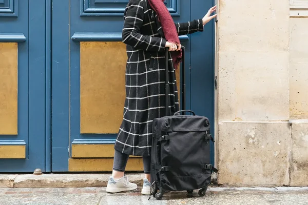 Un expatrié de retour, valise à la main, devant une porte bleue, symbole du retour au pays.