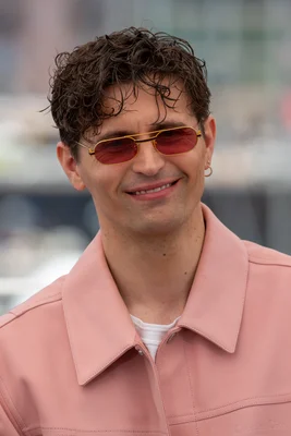 Raphaël Quenard souriant, portant des lunettes de soleil dorées.