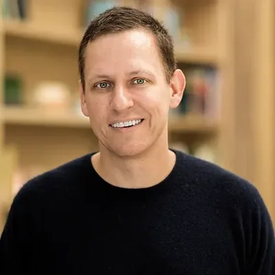Portrait de Peter Thiel en pull sombre, souriant devant des étagères.
