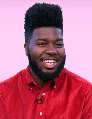 Portrait de Khalid, chemise rouge, souriant devant un fond rose.