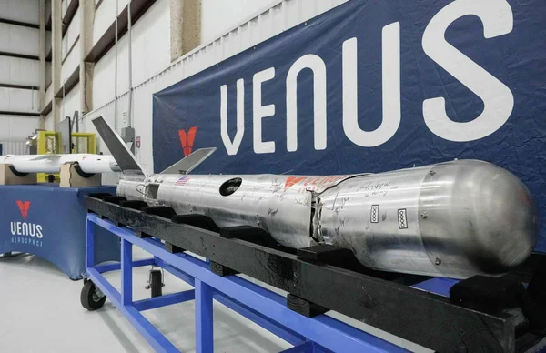 Fuselage de fusée Venus Aerospace, abîmé et signé, exposé dans un hangar avec la bannière de l'entreprise.