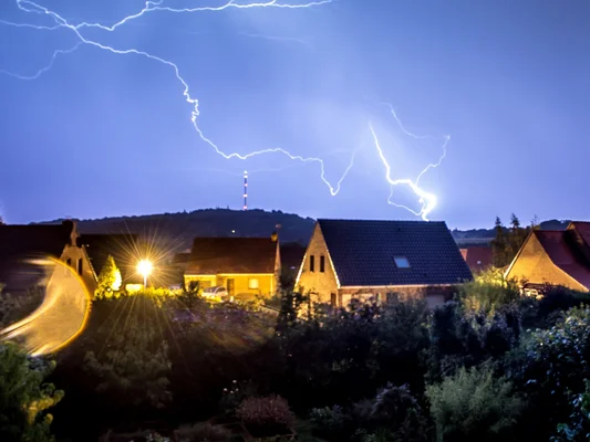 Orage dans le Sud-Ouest : impact de foudre au-dessus d'un quartier résidentiel, avec des traînées de phares sur une route.