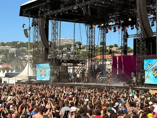 Concert du Delta Festival : la foule lève les mains et les téléphones vers la scène, devant un paysage côtier.