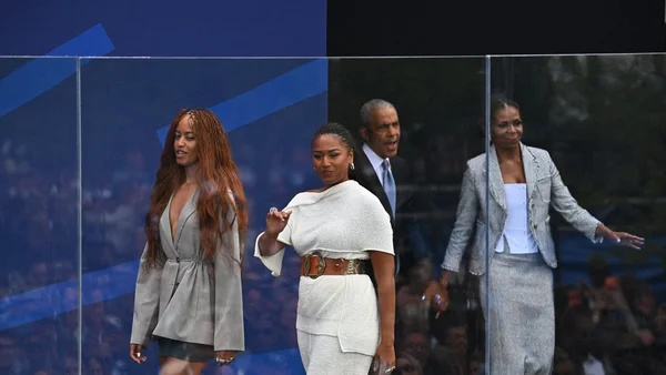 Barack Obama et Michelle Obama marchant sur une scène avec deux autres personnes derrière une barrière transparente.