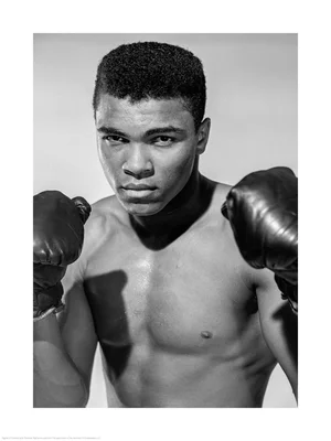 Portrait de Mohamed Ali torse nu, gants aux poings, regard intense.