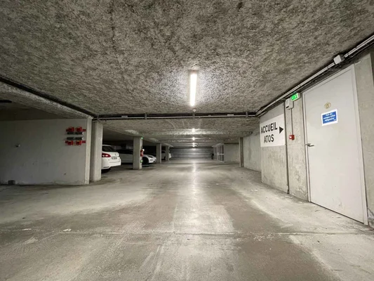 Parking souterrain avec voitures garées et une porte d'accueil visible.