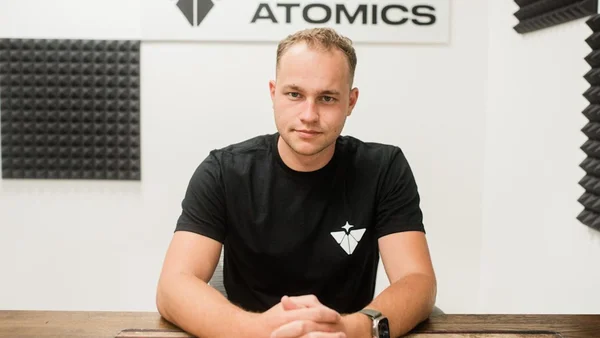 Portrait d'un représentant de Valar Atomics dans un bureau équipé de panneaux acoustiques, avec l'enseigne 'ATOMICS' en arrière-plan.