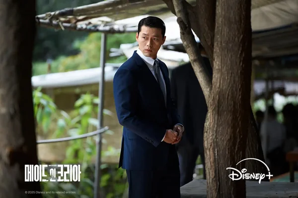 Image promotionnelle de la série Disney+ 'Made in Korea' mettant en vedette l'acteur Hyun Bin. L'image montre l'acteur dans un costume bleu foncé, tenant une arme à feu, avec un regard intense, évoquant le genre thriller criminel. Les logos de la série et de Disney+ sont visibles.
