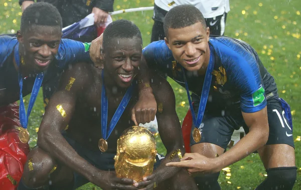 Benjamin Mendy et deux coéquipiers de l'équipe de France célèbrent leur victoire en soulevant le trophée de la Coupe du monde 2018 sur la pelouse, sous une pluie de confettis dorés.