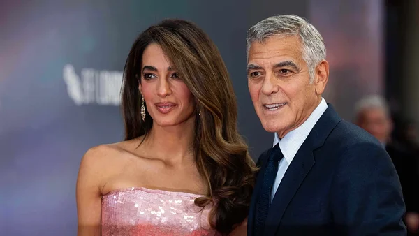 George et Amal Clooney posant ensemble lors d'un événement officiel, elle vêtue d'une robe rose à sequins et lui d'un costume sombre