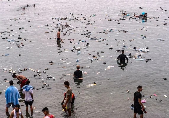 Groupe de migrants nageant et pataugeant dans une eau polluée par des déchets plastiques, près de Ceuta, en 2026