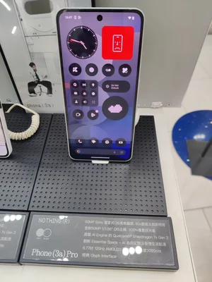 Un Nothing Phone (3a) Pro présenté sur un support de vente, avec son interface Glyph et son panneau de contrôle à l'écran, accompagné d'une affiche détaillant ses caractéristiques techniques.