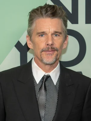 Portrait d'Ethan Hawke en costume noir, chemise blanche et cravate à motifs, devant un fond vert clair, issu de sa page Wikipédia.