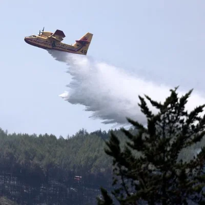 Canadair jaune numéro 48 larguant un écran d'eau ou de retardant au-dessus d'une forêt en flammes, illustrant les moyens de lutte contre les incendies souvent causés par négligence humaine