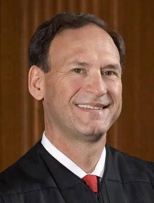Portrait officiel du juge Samuel Alito, souriant, en robe noire, chemise blanche et cravate rouge, sur fond brun.
