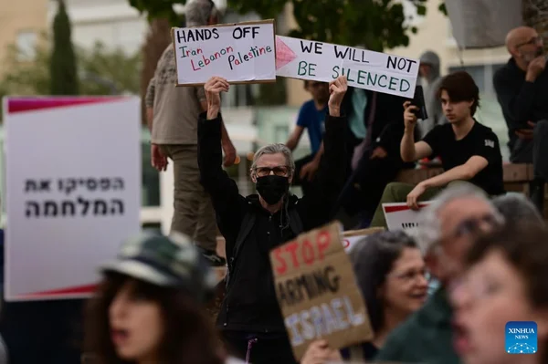 Un manifestant à Tel Aviv tient des pancartes « HANDS OFF Iran Lebanon Palestine » et « WE WILL NOT BE SILENCED », entouré d'autres participants brandissant des affiches en hébreu et en anglais.