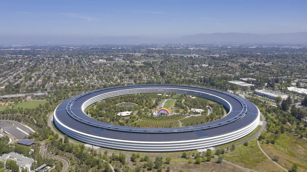Vue aérienne du campus Apple Park à Cupertino, avec son bâtiment principal en forme d'anneau entouré de verdure et de paysages suburbains.