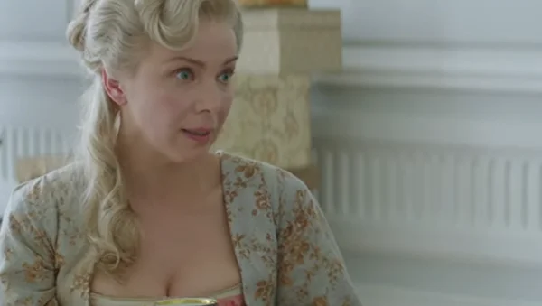 Natalia Dontcheva, actrice franco-bulgare, dans un costume d'époque fleuri et une coiffure du XVIIIe siècle, regardant de côté, dans une scène du film Mademoiselle de Joncquières.