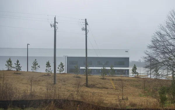 Vue extérieure d'un grand bâtiment industriel gris portant le numéro 1365, situé sur East Hightower Road à Social Circle, en Géorgie, que ICE prévoit de transformer en centre de détention pour 8 500 à 10 000 personnes, sous un ciel couvert.
