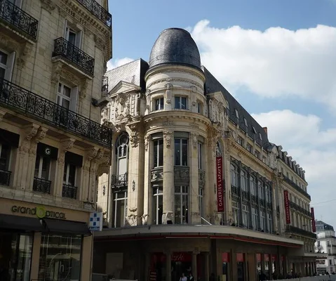 Façade historique du BHV d'Angers, un grand bâtiment orné avec une tourelle à dôme, abritant les Galeries Lafayette, sous un ciel partiellement nuageux.