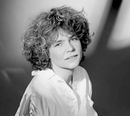 Portrait en noir et blanc de Sabine Paturel, cheveux courts et bouclés, portant une chemise claire à col, regardant légèrement hors cadre.