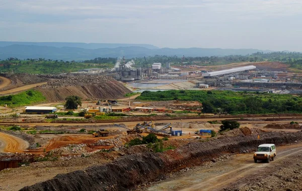 Vue large de l'installation de traitement de la mine de cuivre et de cobalt de Tenke Fungurume, au nord-ouest de Lubumbashi, avec des machines lourdes, des routes en terre et des cheminées émettant de la vapeur.